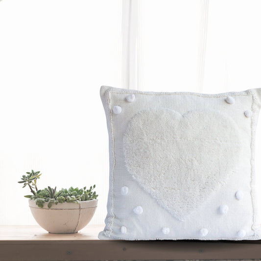 Close-up of a white tufted heart pillow cover with pom-pom details.